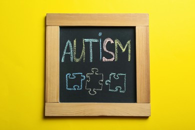 Photo of Chalkboard with word Autism and drawn jigsaw puzzle pieces on yellow background, top view