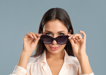 Beautiful young woman wearing sunglasses on grey background