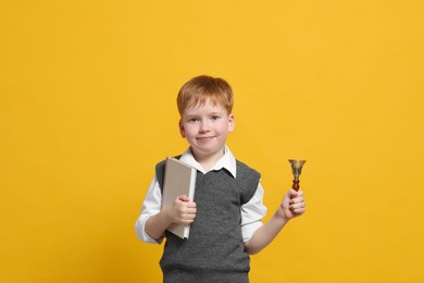 Photo of Pupil with school bell and book on orange background