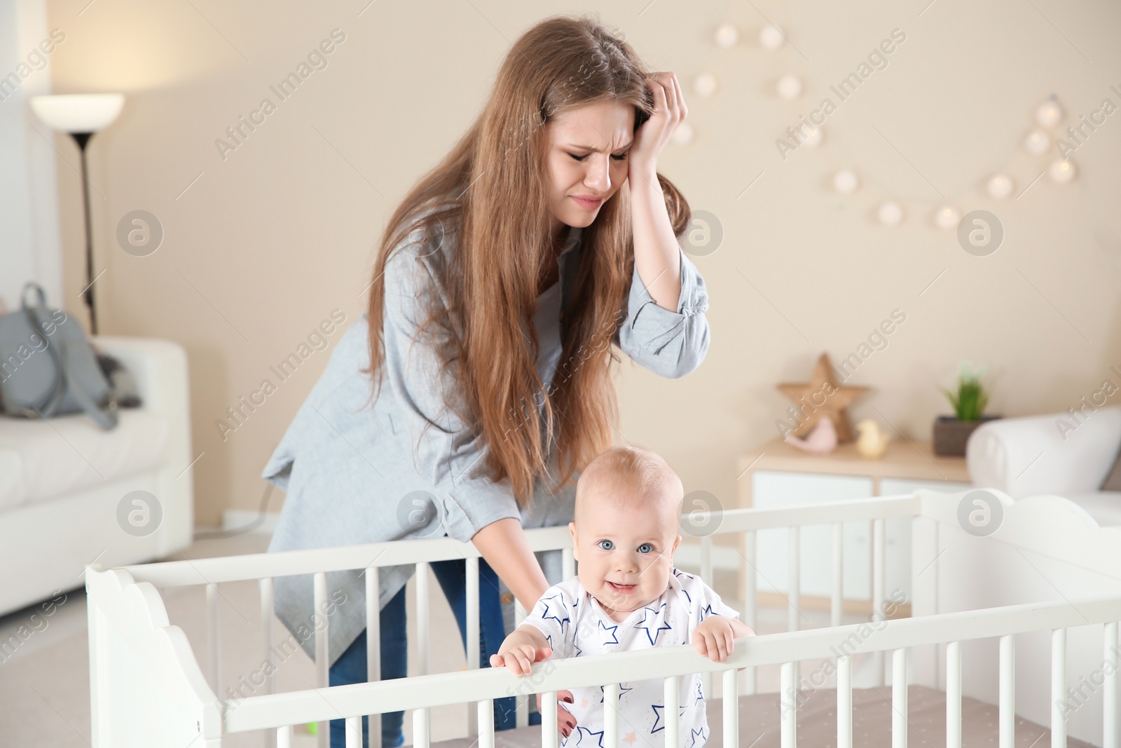 Photo of Cute baby girl in crib and young mother suffering from postnatal depression at home