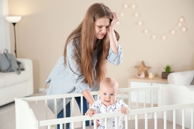 Cute baby girl in crib and young mother suffering from postnatal depression at home