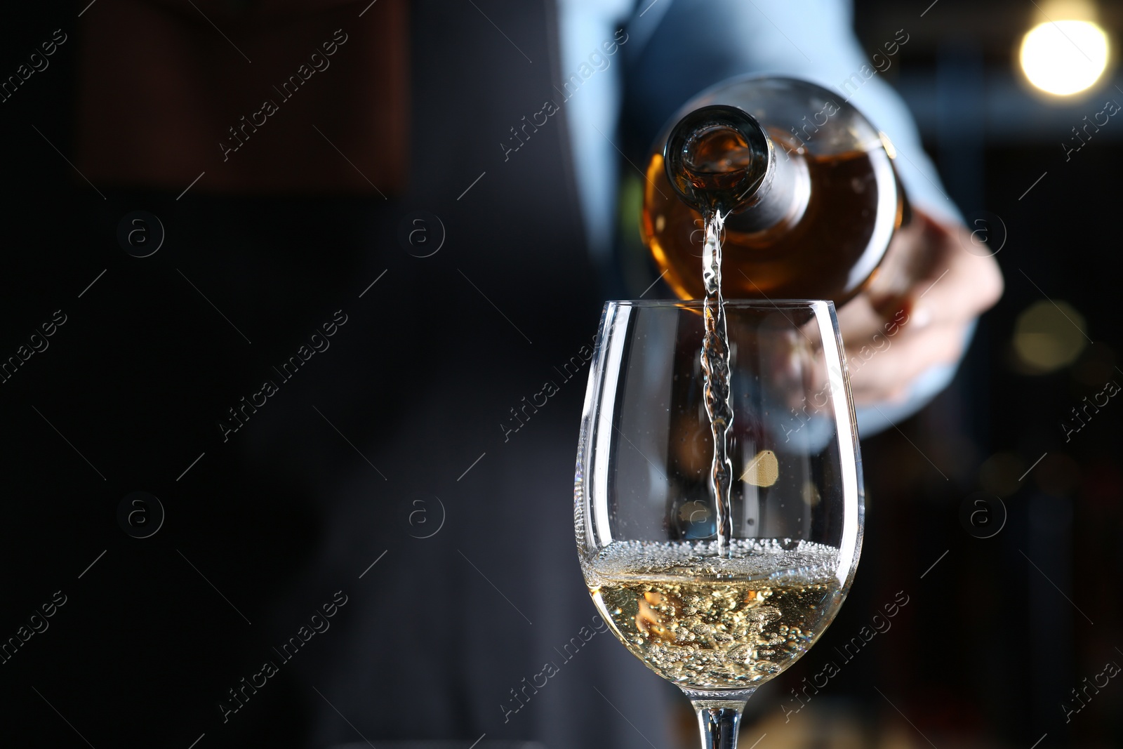 Photo of Bartender pouring white wine from bottle into glass indoors, closeup. Space for text