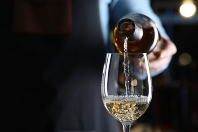 Bartender pouring white wine from bottle into glass indoors, closeup. Space for text