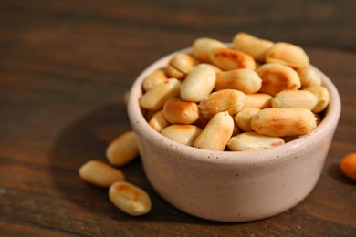 Photo of Roasted peanuts in bowl on wooden table, closeup. Space for text