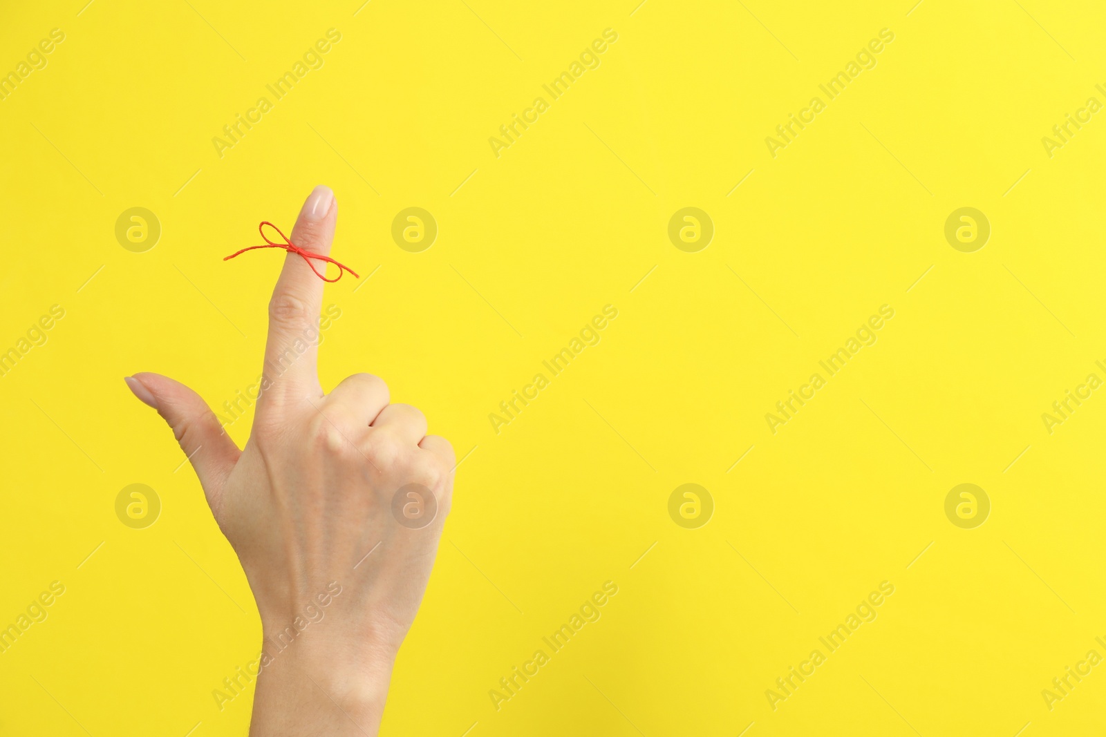 Photo of Woman showing index finger with tied red bow as reminder on yellow background, closeup. Space for text