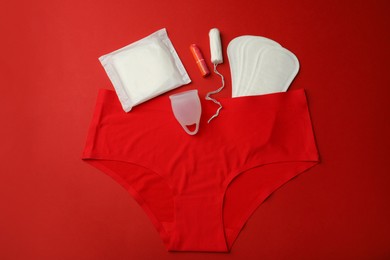 Photo of Menstrual cup with other feminine hygiene products and panties on red background, flat lay
