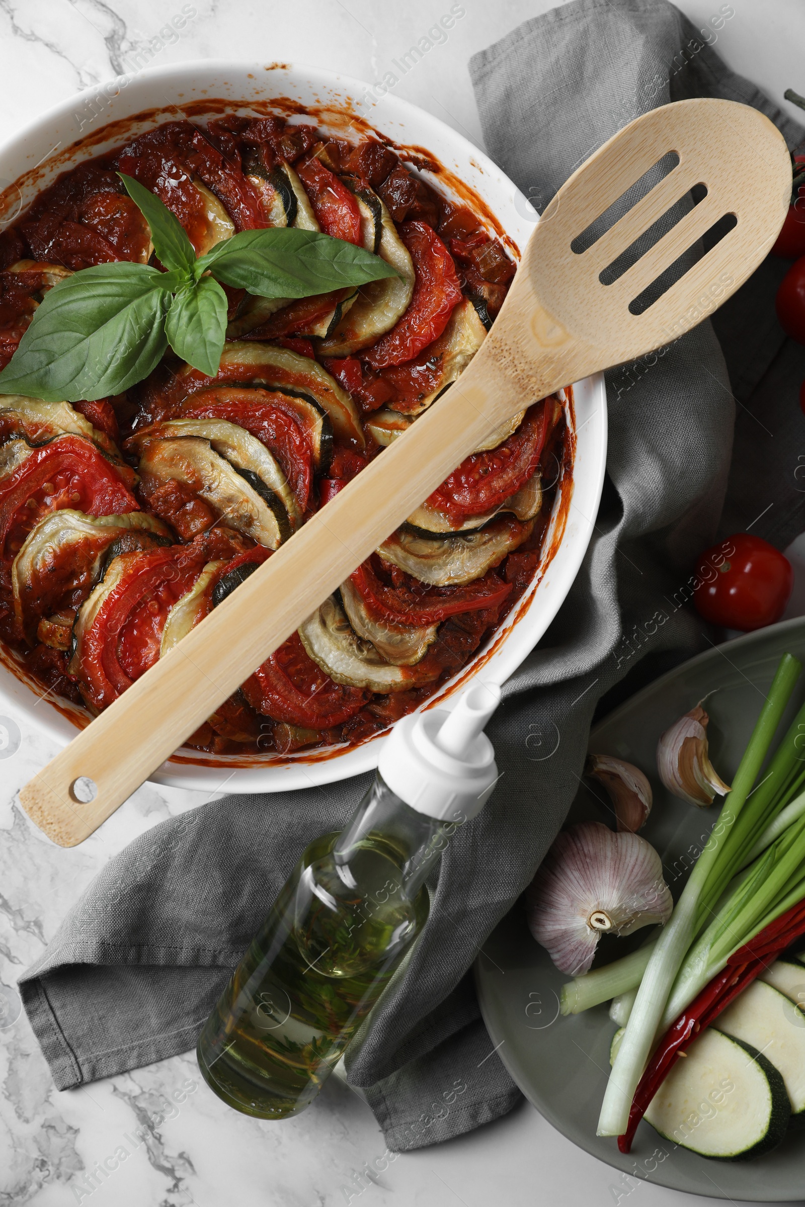 Photo of Delicious ratatouille and ingredients on white marble table, flat lay