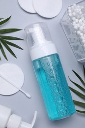 Photo of Bottle of face cleansing product, leaves, cotton buds and pads on light grey background, flat lay with space for text