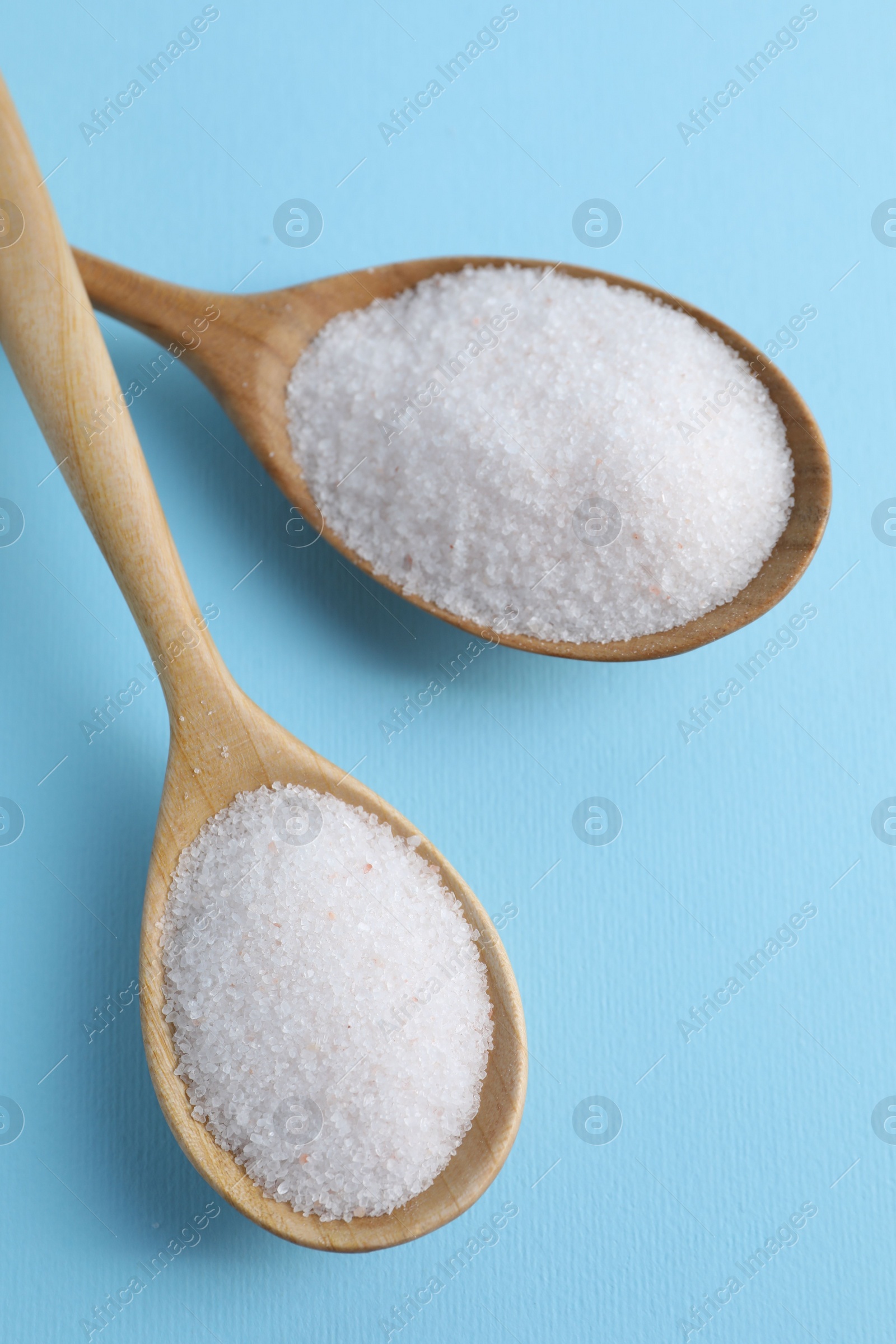 Photo of Organic white salt in spoons on light blue background, top view