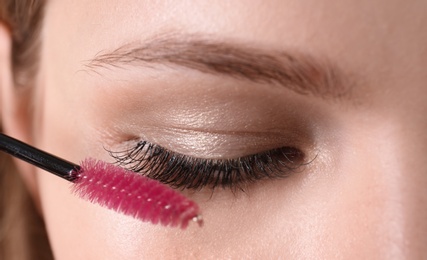 Photo of Attractive young woman applying mascara on her eyelashes, closeup