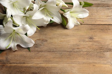 Photo of Beautiful white lily flowers on wooden table, space for text
