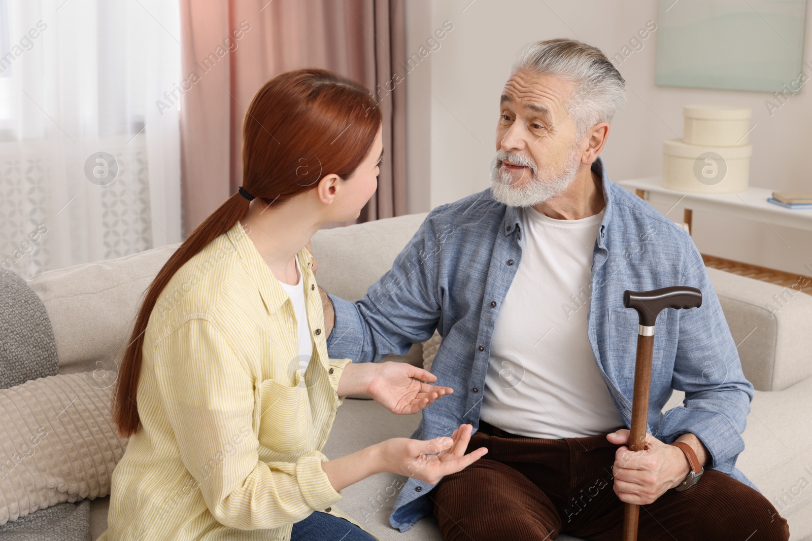 Photo of Caregiver and senior man with walking cane on sofa at home