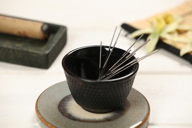 Photo of Bowl with acupuncture needles on white wooden table, closeup
