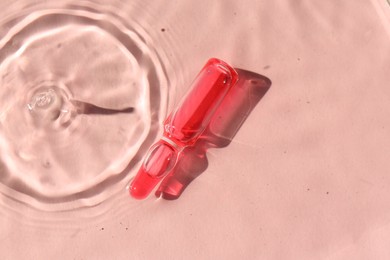 Skincare ampoule in water on pink background, top view