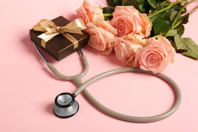 Photo of Stethoscope, gift box and flowers on pink background. Happy Doctor's Day