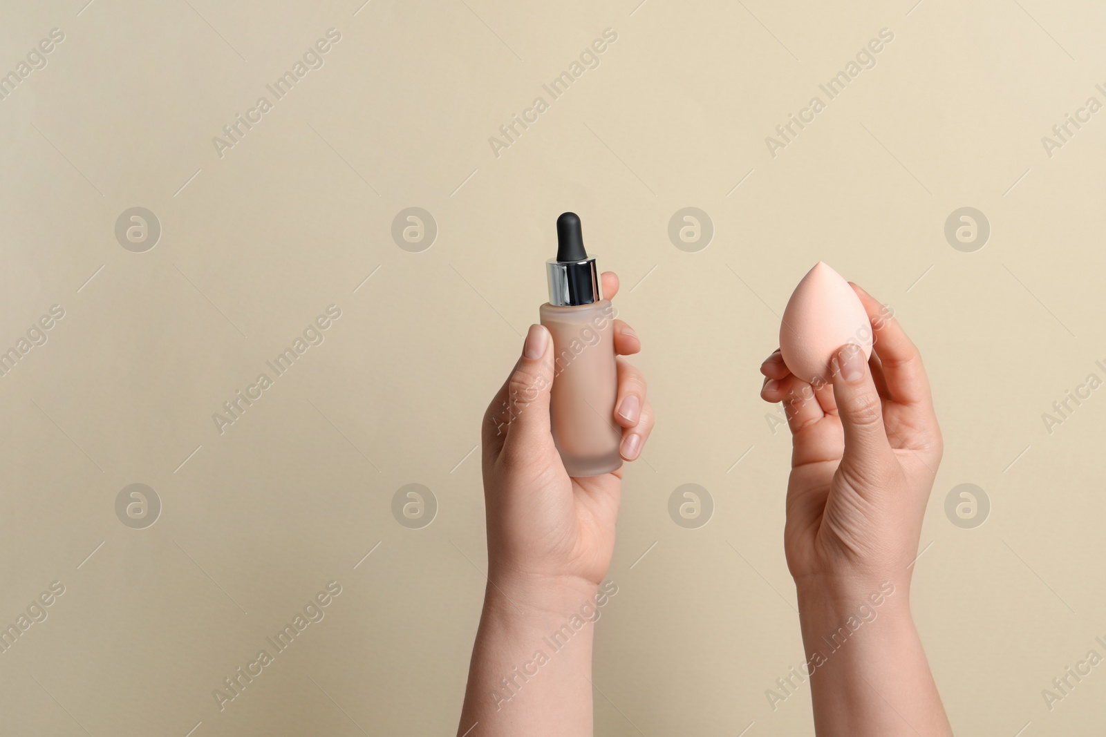 Photo of Woman holding bottle with skin foundation and makeup sponge on beige background, closeup. Space for text