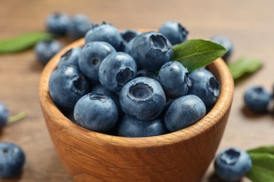 Photo of Bowl of tasty fresh blueberries with green leaves on table, closeup