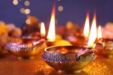 Photo of Diwali celebration. Diya lamps on shiny golden table against blurred lights, closeup