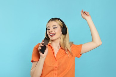Happy woman in headphones enjoying music and singing into smartphone on light blue background
