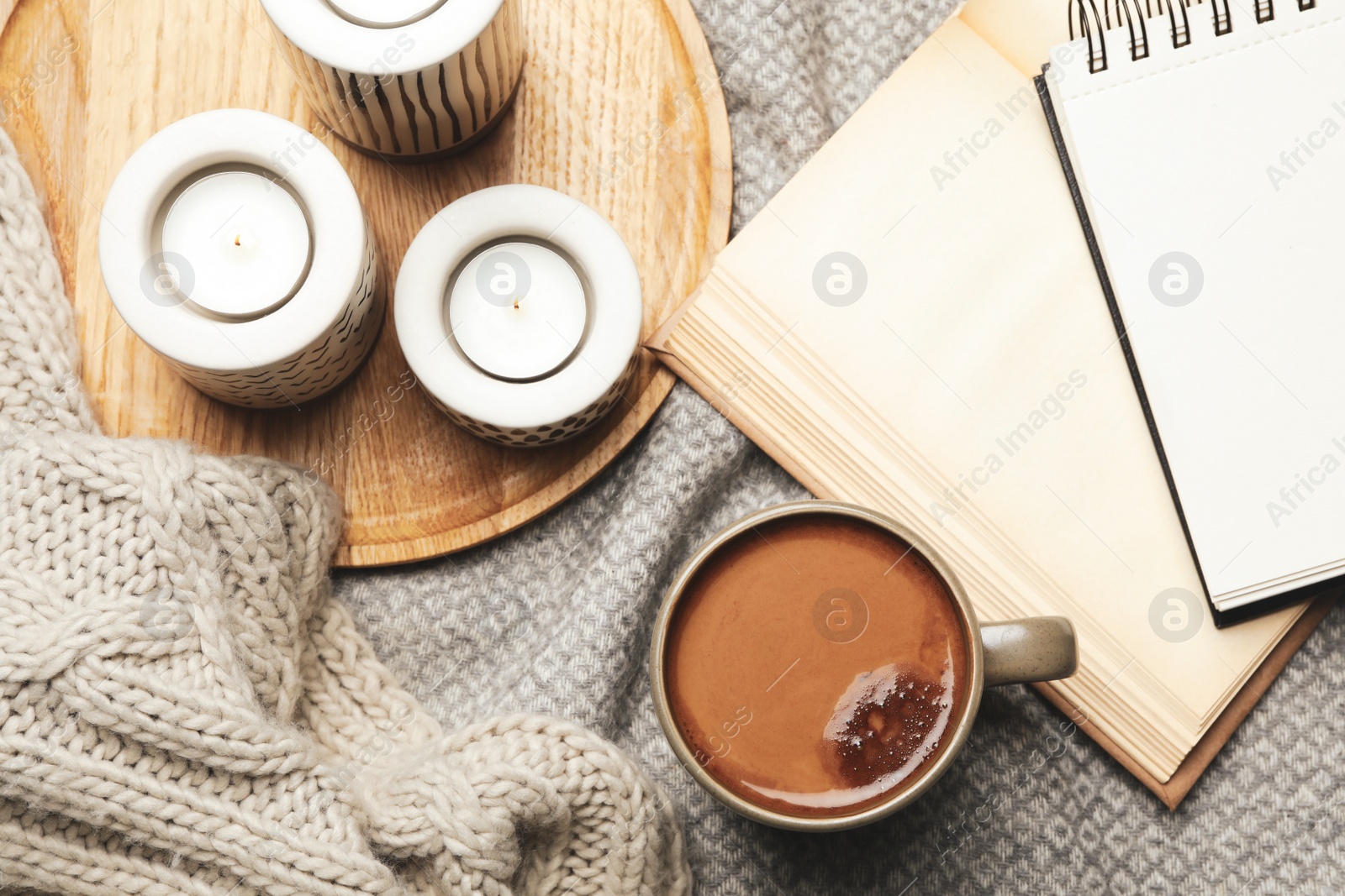 Photo of Cup of delicious hot winter drink and candles on grey fabric, flat lay. Winter drink