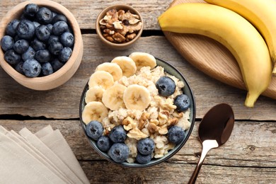 Photo of Tasty oatmeal with banana, blueberries and walnuts served in bowl on wooden table, flat lay