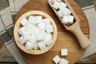 Photo of White sugar cubes in bowl and scoop on wooden table, top view