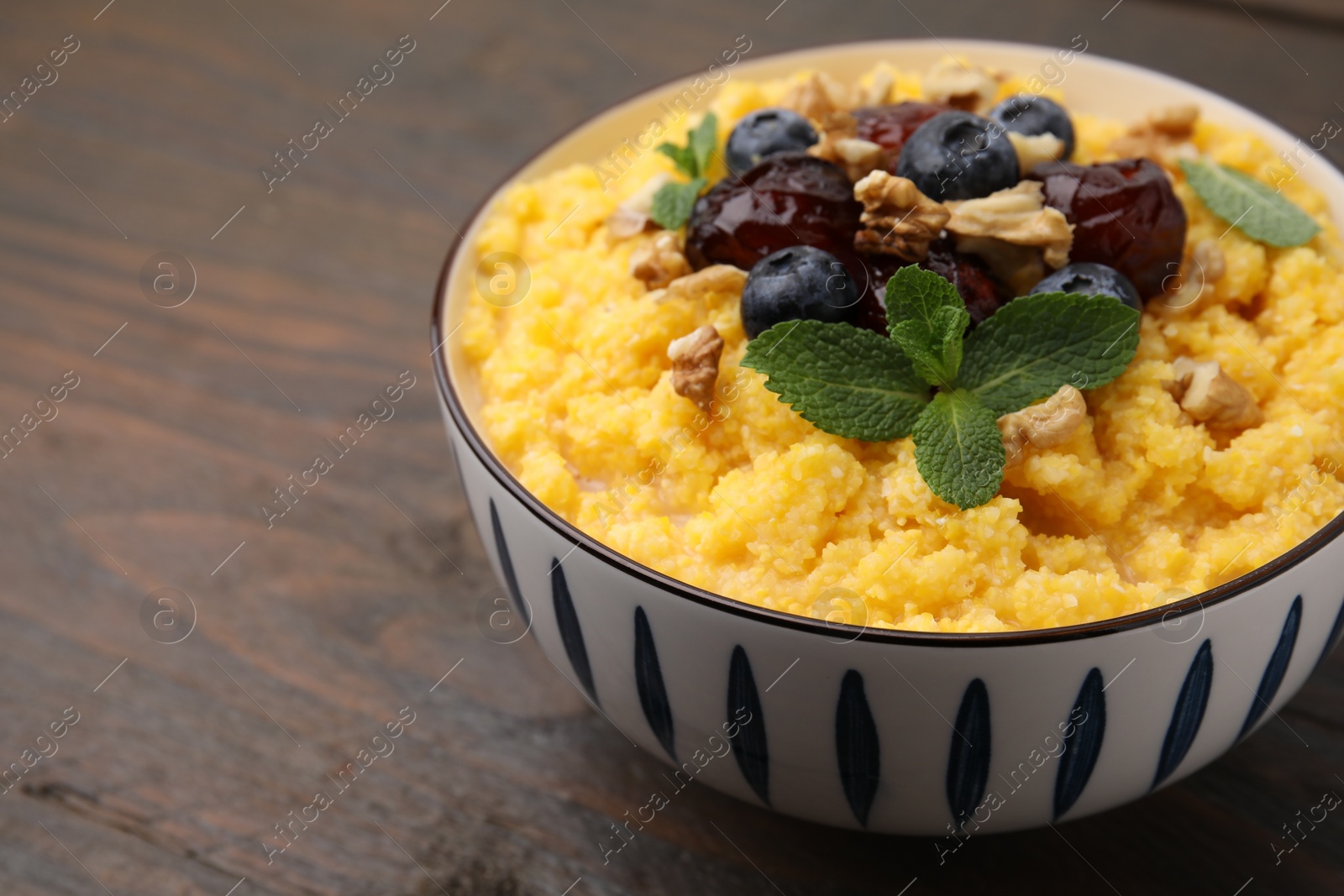 Photo of Tasty cornmeal with blueberries, dates, walnuts and mint in bowl on wooden table, closeup