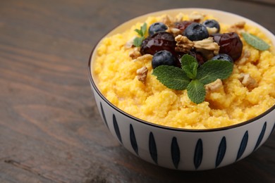 Photo of Tasty cornmeal with blueberries, dates, walnuts and mint in bowl on wooden table, closeup