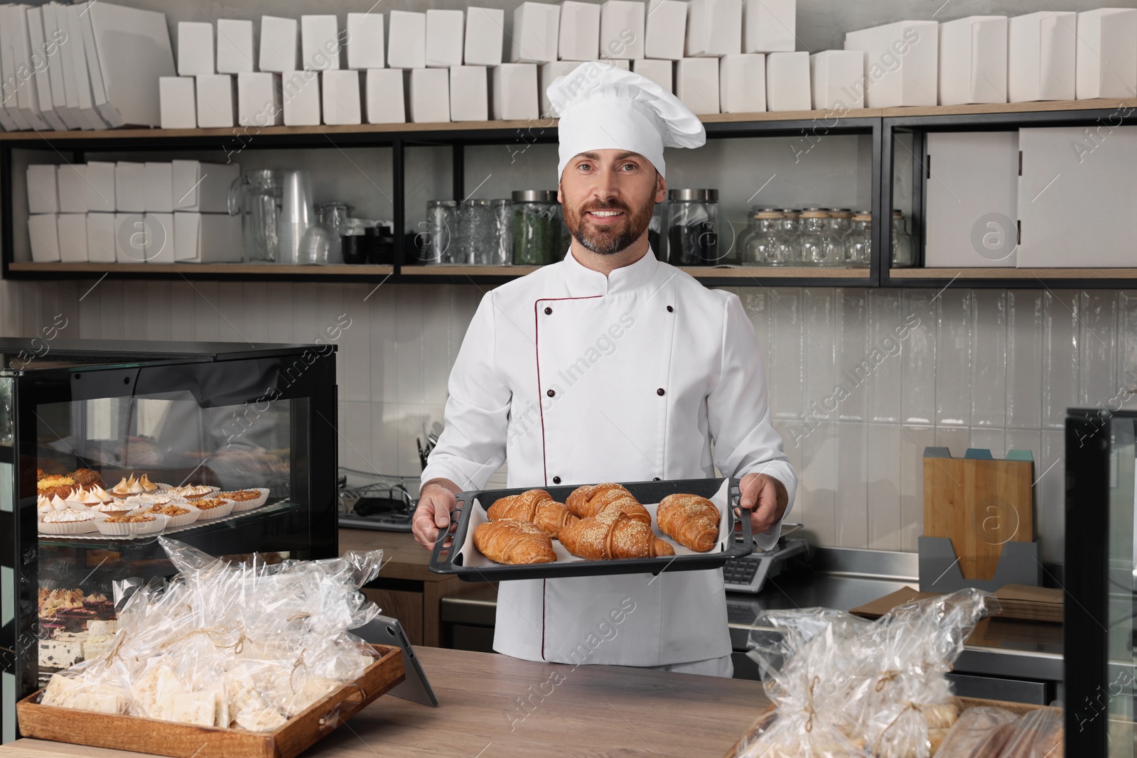 Photo of Professional baker with freshly baked croissants in store