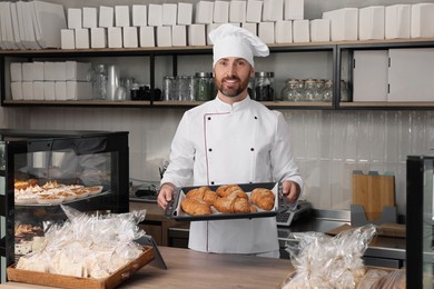 Photo of Professional baker with freshly baked croissants in store