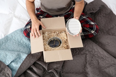 Young man opening parcel in bedroom at home, closeup