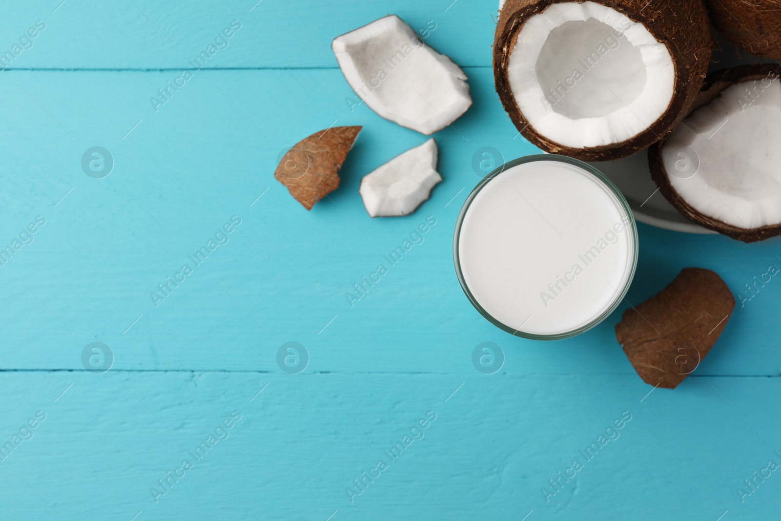 Photo of Glass of delicious vegan milk and coconuts on light blue wooden table, flat lay. Space for text