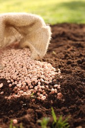 Photo of Granulated fertilizer in sack on soil, closeup