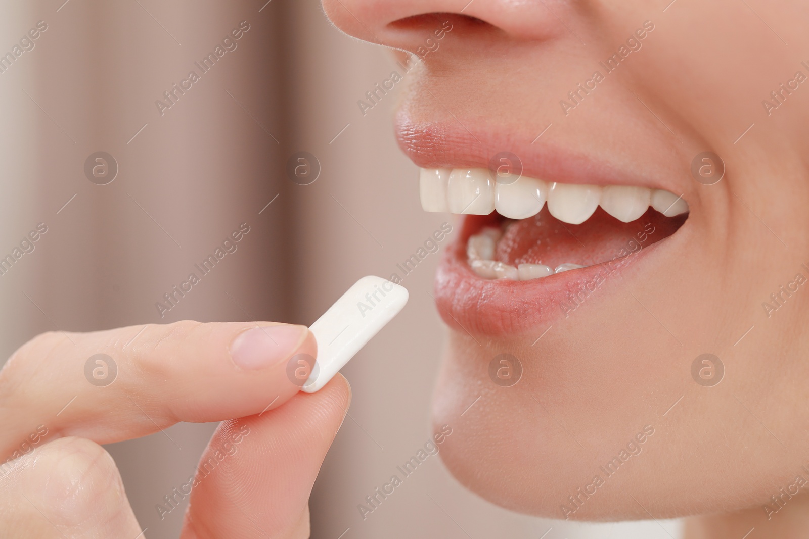 Photo of Woman putting chewing gum into mouth on blurred background, closeup