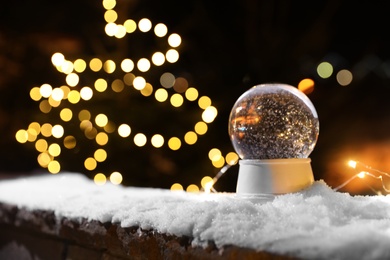 Photo of Snow globe and blurred Christmas lights on background. Space for text