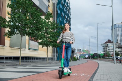 Happy woman riding modern electric kick scooter on city street, space for text