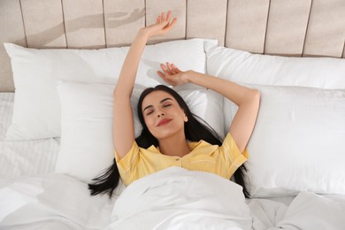Photo of Young woman stretching in bed with white linens at home, above view