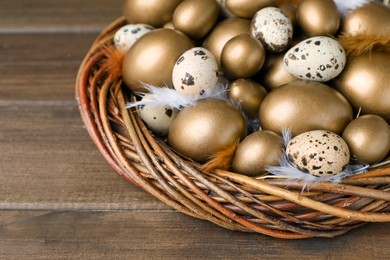 Many golden and quail eggs in nest on wooden table