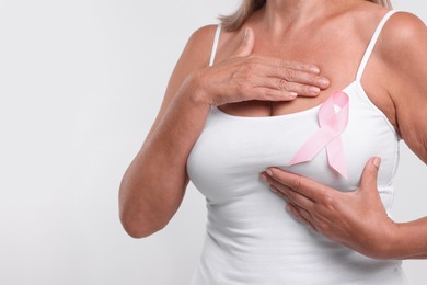 Photo of Woman with pink ribbon on white background, closeup and space for text. Breast cancer awareness