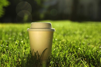 Photo of Cardboard takeaway coffee cup with lid on green grass outdoors, space for text