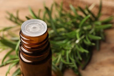 Photo of Bottle with essential oil and fresh rosemary against blurred background, closeup. Space for text