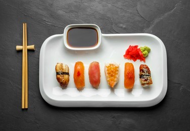 Photo of Plate with delicious nigiri sushi and soy sauce on black table, top view
