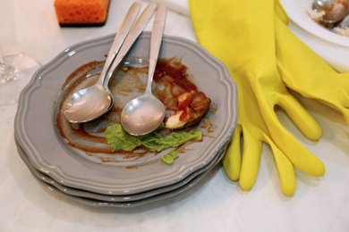 Photo of Dirty dishes and yellow gloves on table, closeup. Mess after new year party