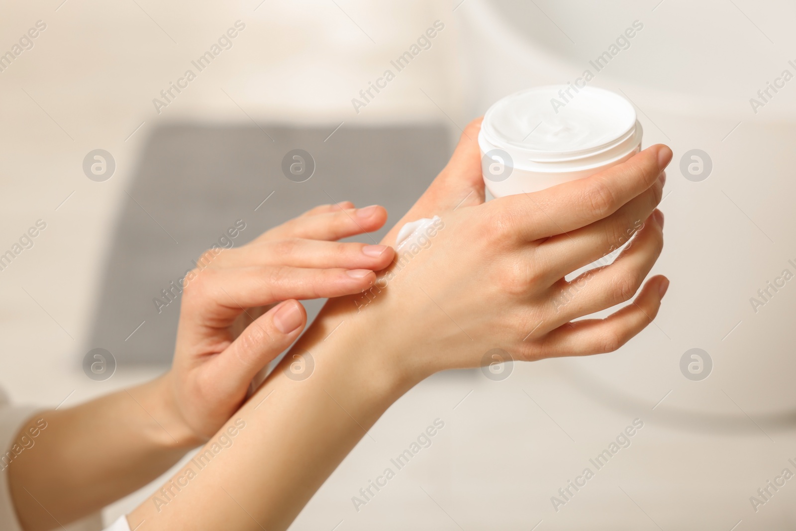 Photo of Young woman applying body cream onto hand indoors, closeup