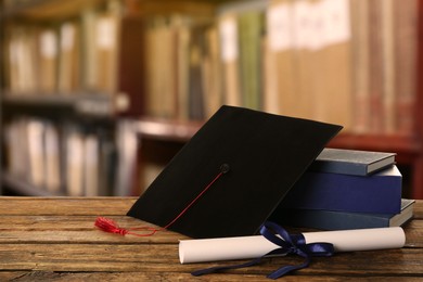 Graduation hat, books and diploma on wooden table in library