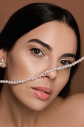 Young woman with elegant pearl jewelry on brown background, closeup