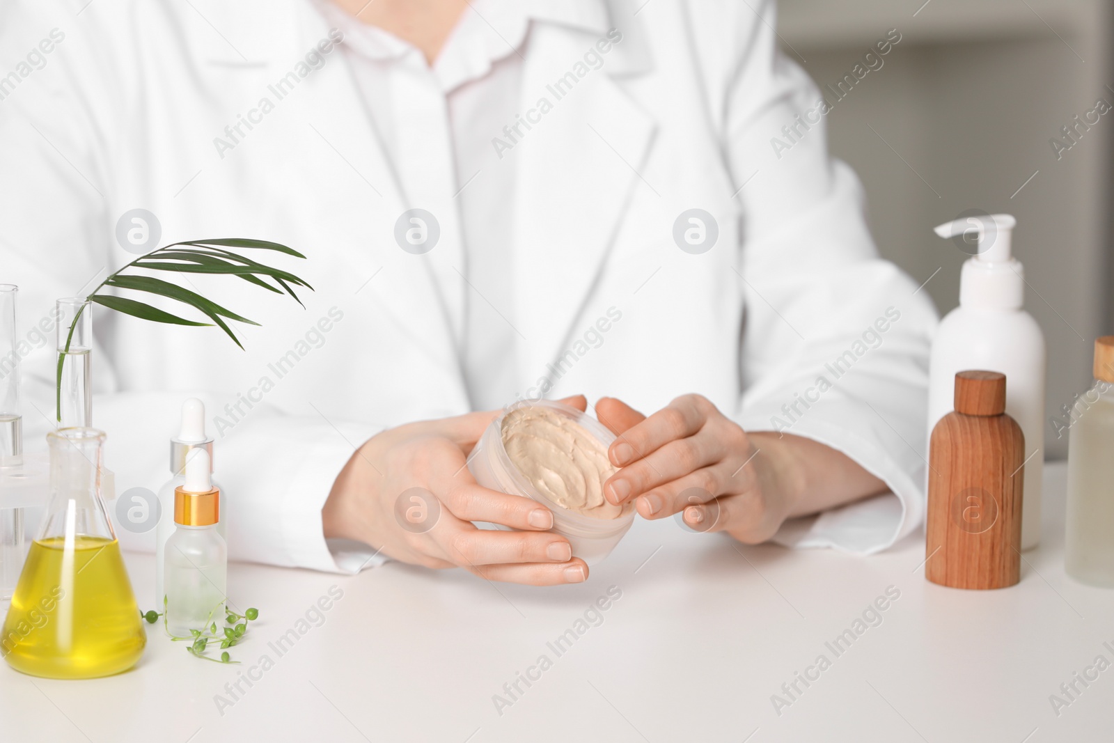 Photo of Dermatologist with jar testing cosmetic product at white table indoors, selective focus