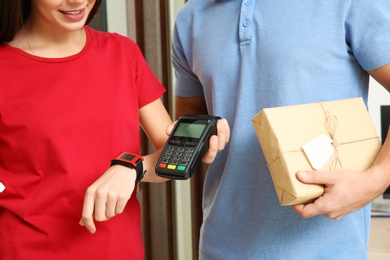 Photo of Woman with smartwatch using terminal for delivery payment indoors, closeup