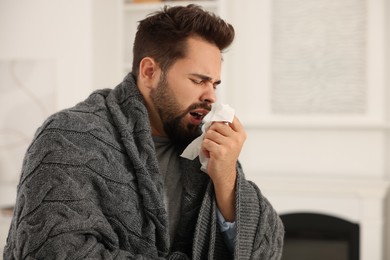 Photo of Sick man wrapped in blanket with tissue at home. Cold symptoms