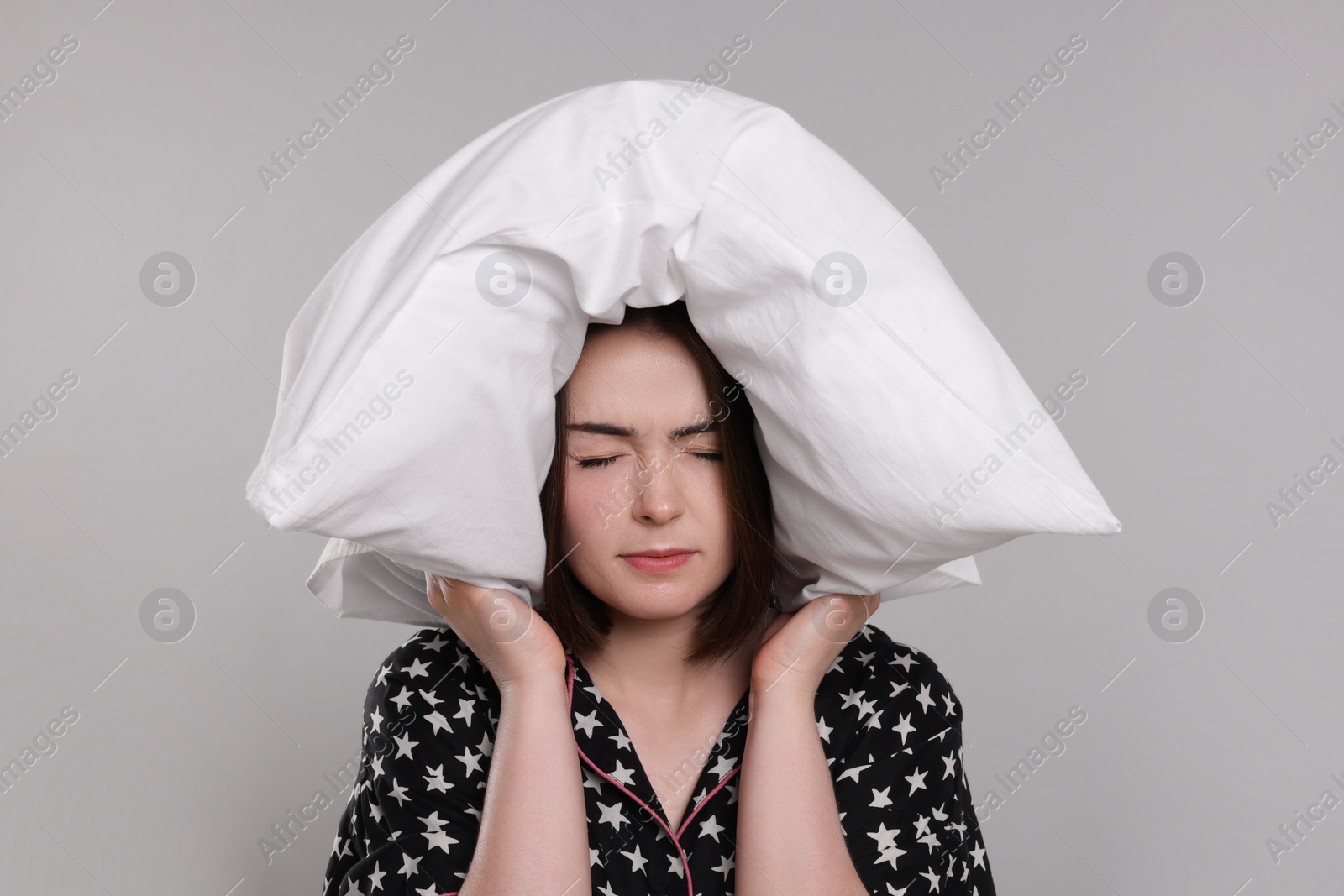 Photo of Unhappy young woman covering ears with pillow on light grey background. Insomnia problem